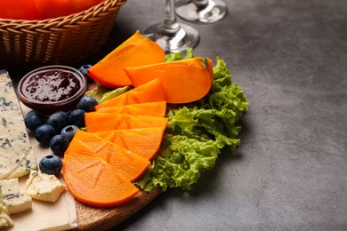 Photo of Delicious persimmon, blue cheese, blueberries and jam served on light grey table. Space for text