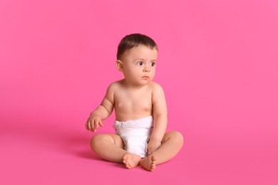Cute baby in dry soft diaper sitting on pink background