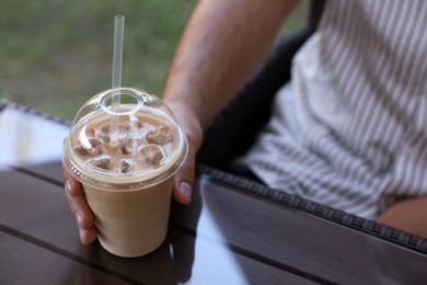 Photo of Man with plastic takeaway cup of delicious iced coffee at table in outdoor cafe, closeup. Space for text