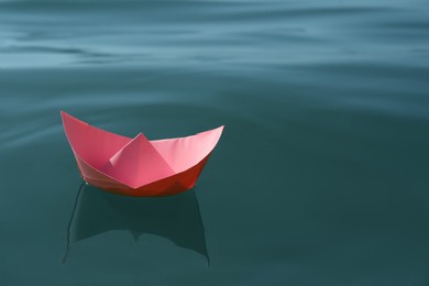 Pink paper boat floating on water surface, space for text