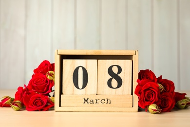 Wooden block calendar with date 8th of March and roses on table against light background, space for text. International Women's Day