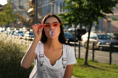 Photo of Beautiful woman in sunglasses blowing gum outdoors, space for text