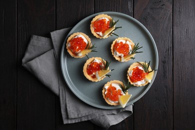 Photo of Delicious tartlets with red caviar and cream cheese served on wooden table, top view