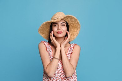 Beautiful young woman with straw hat on light blue background