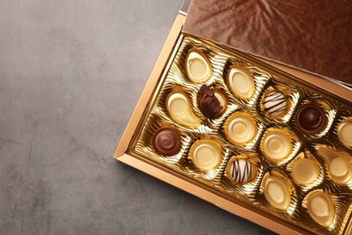 Photo of Partially empty box of chocolate candies on grey background, top view. Space for text