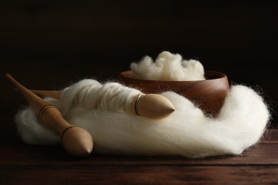 Soft white wool and spindles on wooden table, closeup