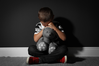 Scared little boy with toy near black wall. Domestic violence concept