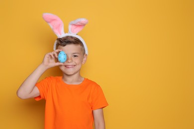Cute little boy in bunny ears holding Easter egg on yellow background. Space for text