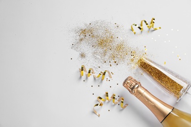 Bottle of champagne, glass with gold glitter and space for text on white background, top view. Hilarious celebration