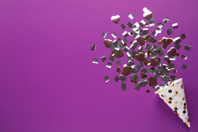 Golden and silver confetti with party cracker on purple background, top view. Space for text