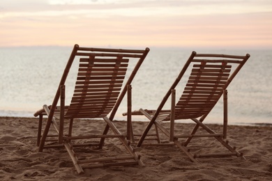 Wooden deck chairs on sandy beach at sunset. Summer vacation