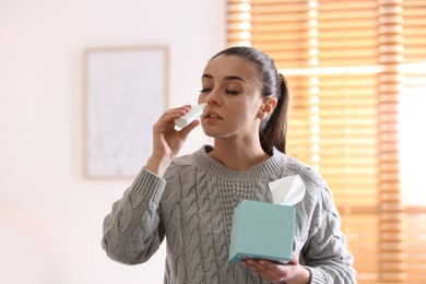 Ill woman with box of paper tissues using nasal spray at home