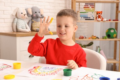 Little boy painting with fingers at white table indoors