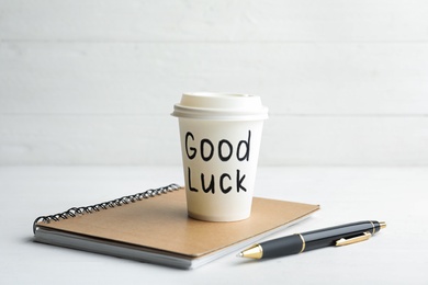Paper coffee cup with phrase GOOD LUCK and stationery on white wooden table