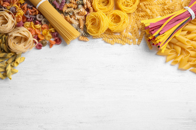 Different types of pasta on white wooden table, flat lay. Space for text