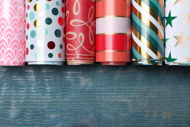 Different colorful wrapping paper rolls on light blue wooden table, flat lay. Space for text