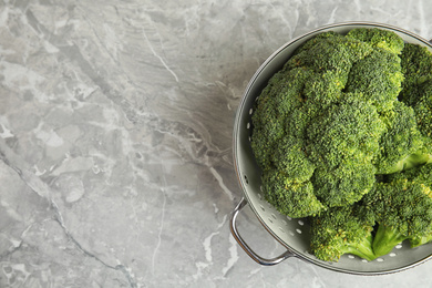 Fresh green broccoli in colander on grey marble table, top view. Space for text