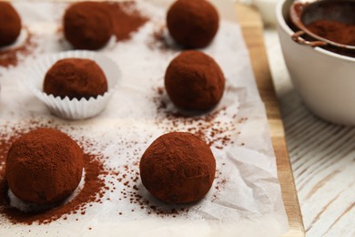 Delicious chocolate truffles powdered with cocoa on white wooden table, closeup