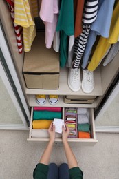 Woman folding clothes in wardrobe drawer indoors, top view. Vertical storage