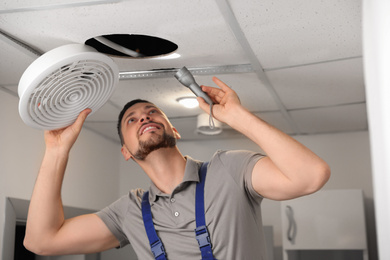 Photo of Repairman with flashlight fixing ventilation system indoors