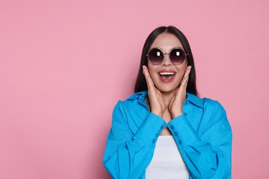 Attractive happy woman in fashionable sunglasses against pink background. Space for text