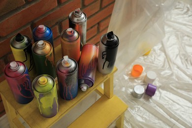 Used cans of spray paints on stand near brick wall indoors. Graffiti supplies