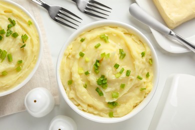 Photo of Bowls of delicious mashed potato with green onion on white table, flat lay