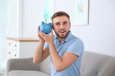 Young man with piggy bank on sofa in living room