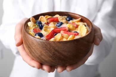 Woman holding bowl of crispy corn flakes with milk and berries, closeup