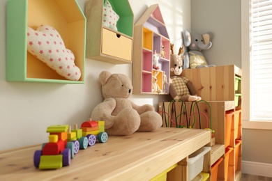 Photo of Colorful wooden toy locomotive and teddy bear on shelf in playroom. Interior design