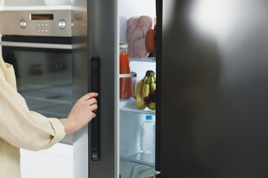 Young woman opening refrigerator indoors, closeup view
