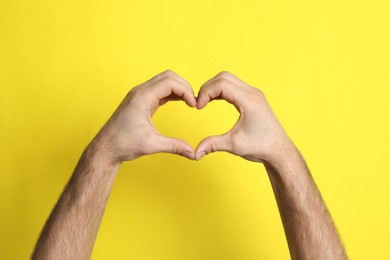 Man making heart with his hands on yellow background, closeup