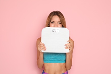 Photo of Happy slim woman satisfied with her diet results holding bathroom scales on color background