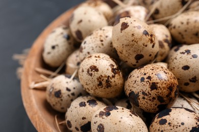 Bowl with quail eggs and straw on black table, closeup