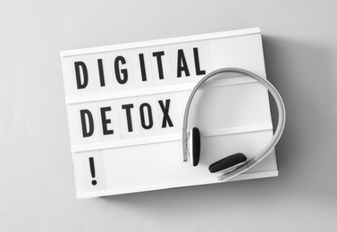 Lightbox with words DIGITAL DETOX and headphones on light grey background, top view
