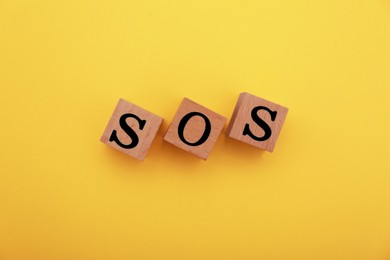 Abbreviation SOS made of wooden cubes on yellow background, top view