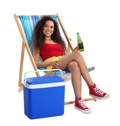 Happy young African American woman with bottle of beer resting in deck chair near cool box on white background