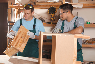 Professional carpenters assembling wooden cabinet in workshop