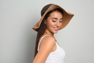 Beautiful young woman wearing straw hat on light grey background. Stylish headdress