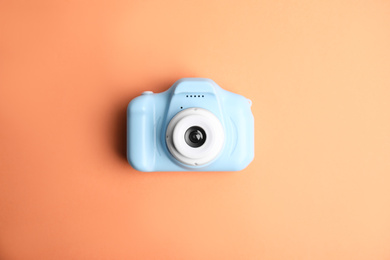 Light blue toy camera on orange background, top view. Future photographer