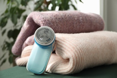 Photo of Modern fabric shaver and woolen sweaters indoors, closeup