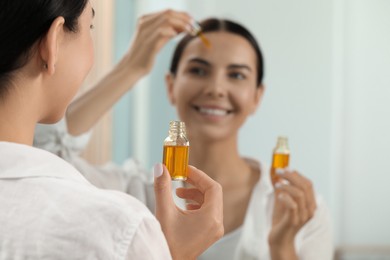 Young woman with bottle of essential oil near mirror, closeup