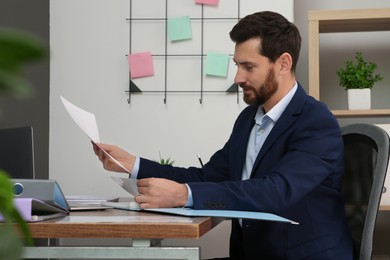 Photo of Businessman putting document into punched pocket at wooden table in office