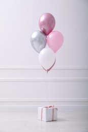 One gift box and balloons near white wall in room