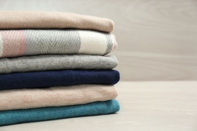 Photo of Stack of cashmere clothes on wooden table. Space for text