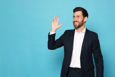 Smiling bearded man in suit showing hand on light blue background. Space for text