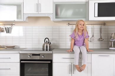 Photo of Cute little girl near oven in kitchen