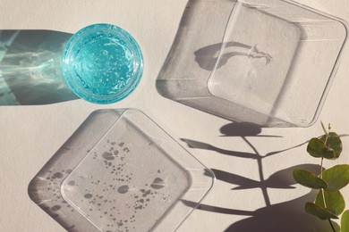 Jar and samples of transparent cosmetic gel on light table, flat lay