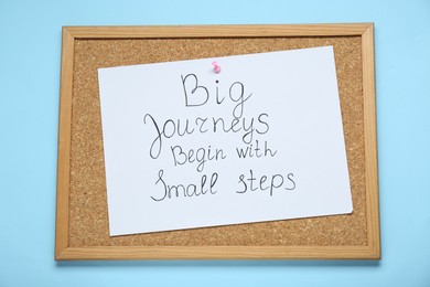 Photo of Corkboard with pinned message Big Journeys Begin With Small Steps on light blue background, top view. Motivational quote