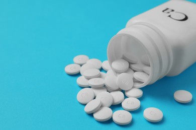 Overturned bottle of calcium supplement pills on light blue background, closeup. Space for text
